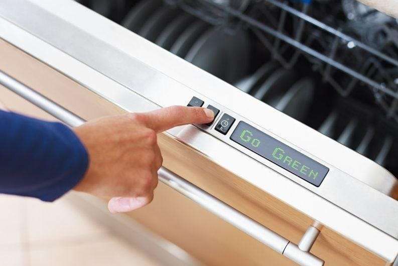 A person’s hand is pressing a button on a dishwasher. The dishwasher display screen shows the message “Go Green” and features the Greenlink option. Plates are visible inside the open dishwasher.