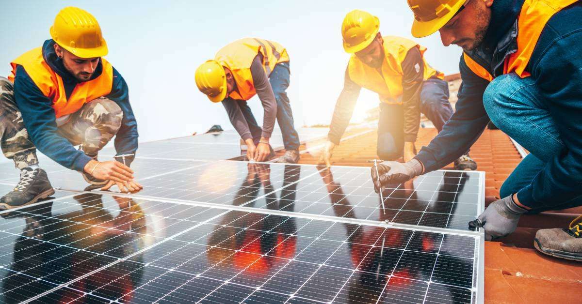 A group of four workers in yellow hardhats and reflective vests meticulously working to install a set of solar panels.