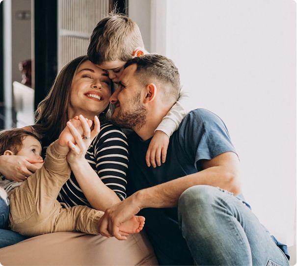 A happy group sits together indoors, smiling and cuddling closely. Two young children embrace their parents, who are holding hands and laughing with joy in Rockford Illinois, where commercial solar and battery storage solutions are growing in popularity.