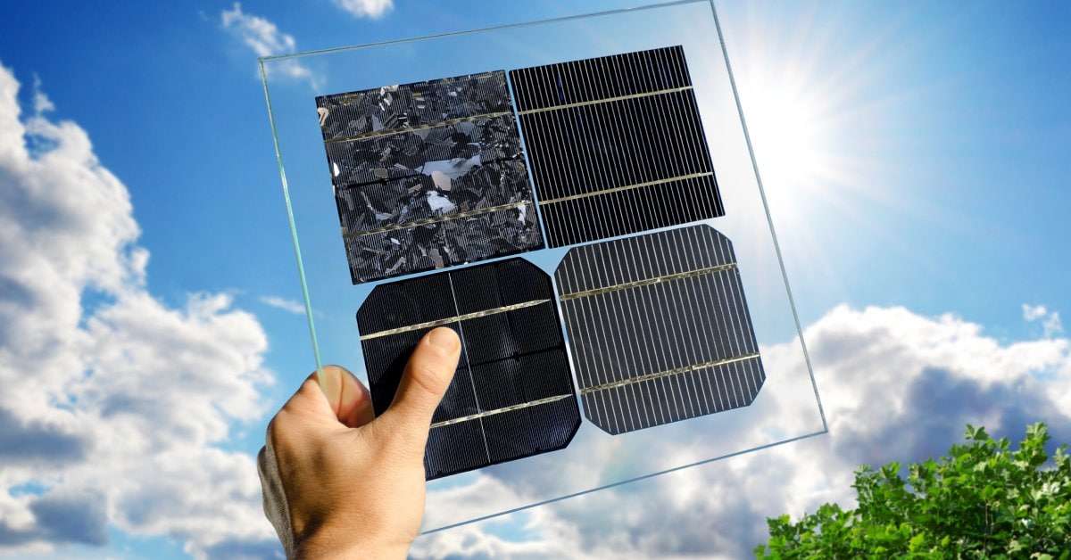 A hand holding up a clear glass panel, with different samples of solar cells, up to the bright, shining sun.